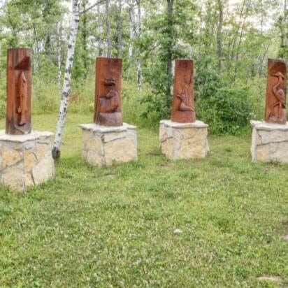 4 wooden logs with animals sculpted into them standing upright on large cubic rocks