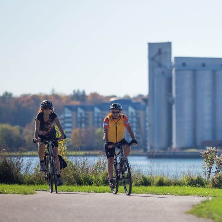 2 people biking on a trail, a river in the background