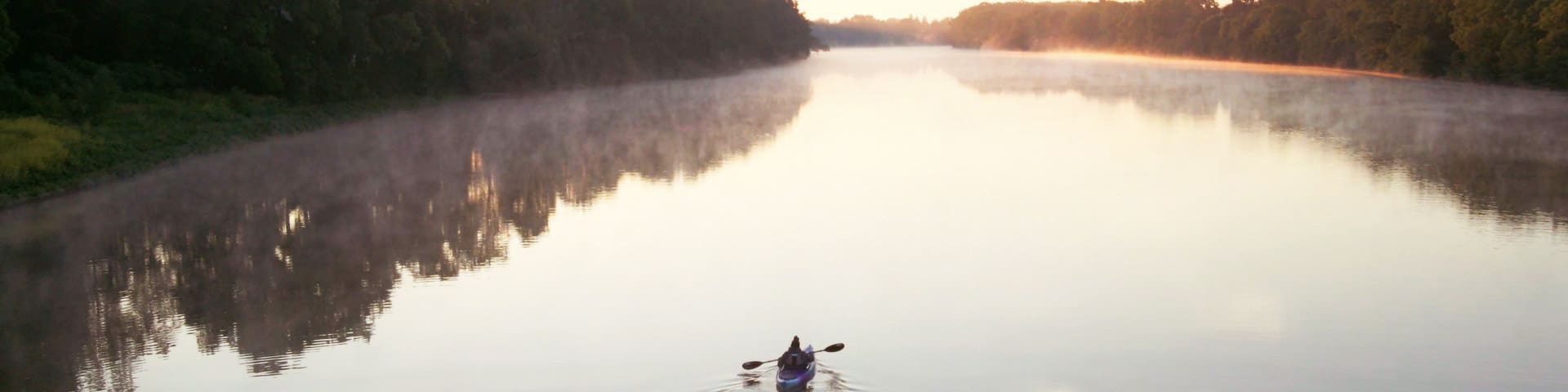 Two people canoe down the foggy Grand River at sunrise